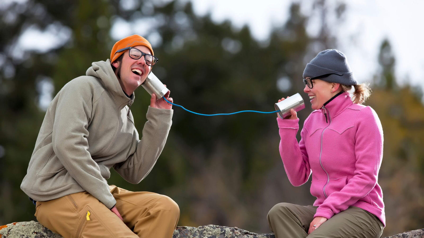 Two people using metal cans as makeshift phones with string.