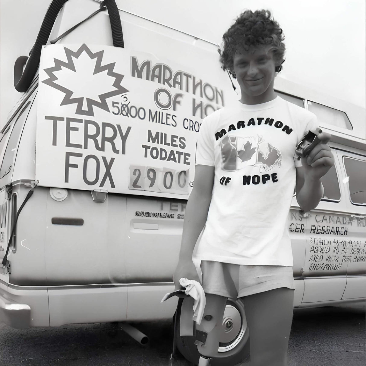 Person wearing a 'Marathon of Hope' shirt standing in front of a van with Terry Fox fundraising sign.