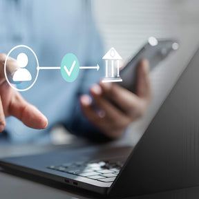 Person using a smartphone with a laptop in the foreground, symbolizing digital identity verification.