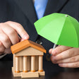 Person holding a green umbrella over a small model of a bank building