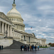 The U.S. Capitol building with people gathered on the steps under a cloudy sky.
