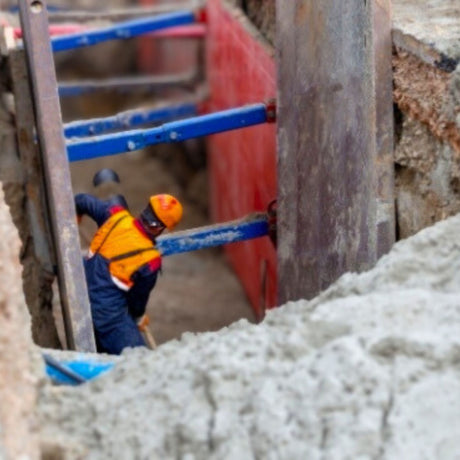 Person in safety gear working on a construction site with concrete and tools.