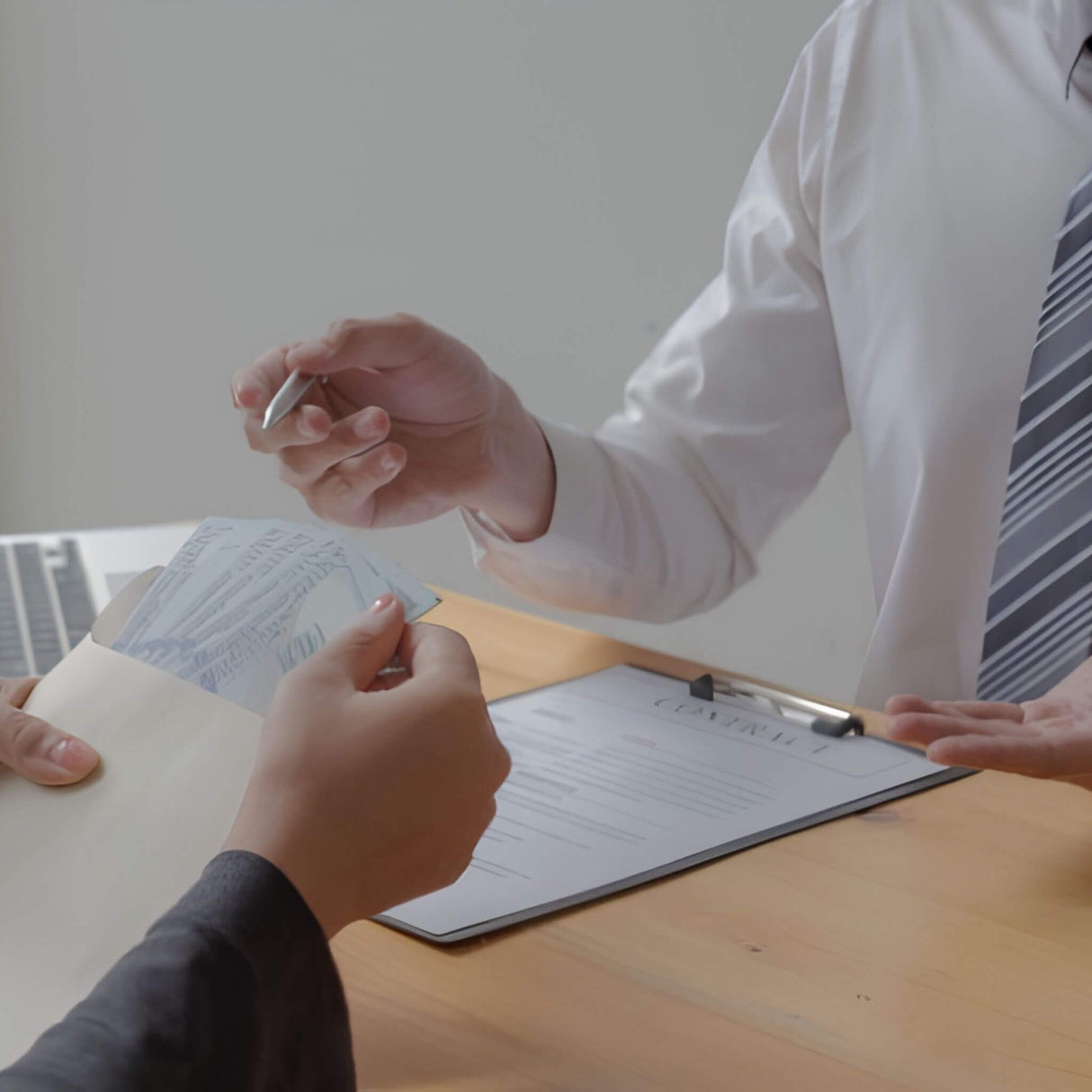 Two people at a desk with a laptop and documents, one person handing over a pen to the other.
